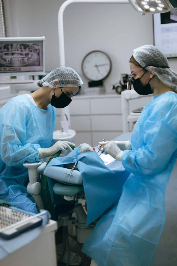 Dva zubní profesionálové v modrých peelingech a maskách provádějí zákrok v prostředí stomatologické kliniky.